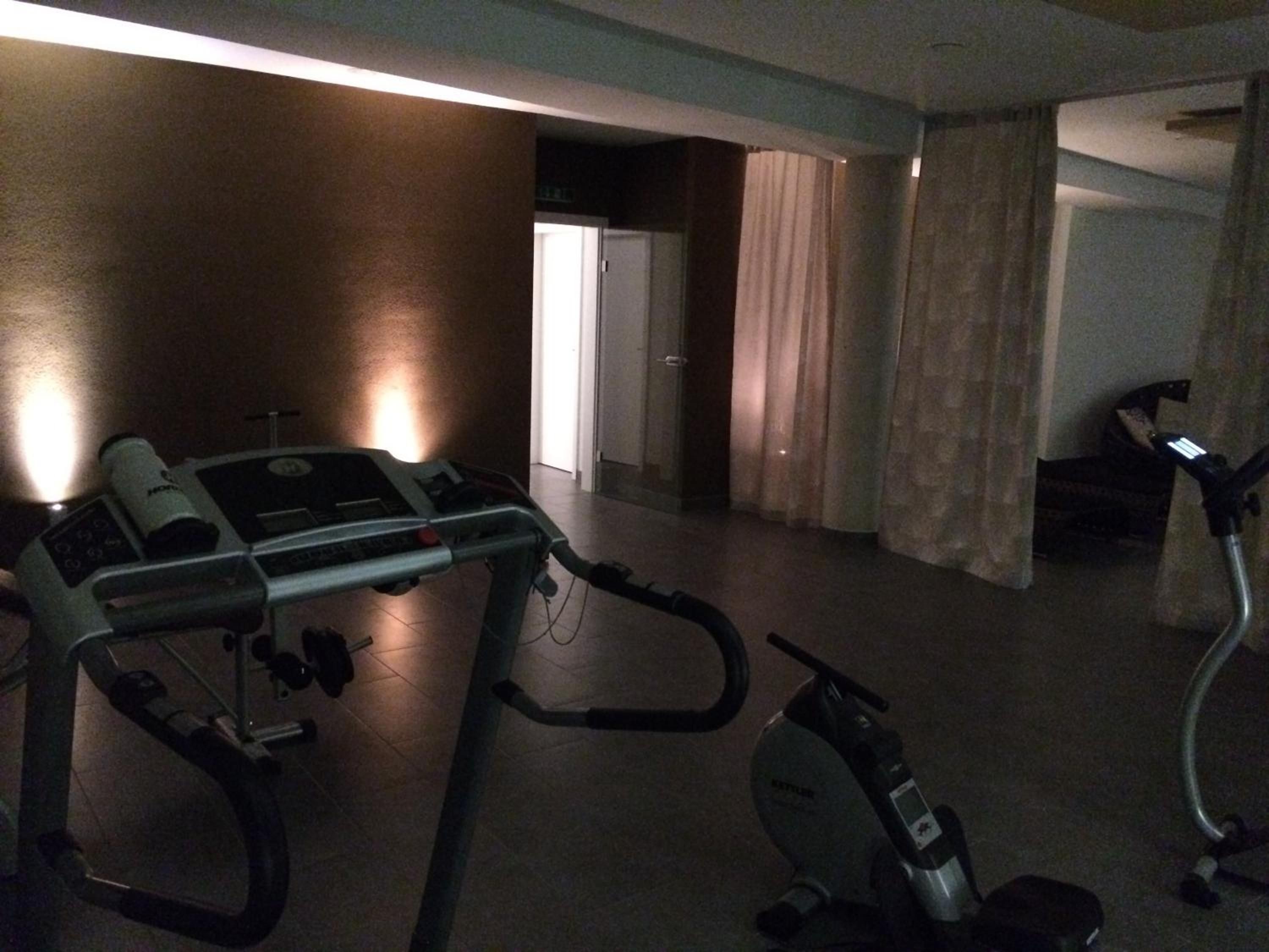 Une pièce équipée d’un tapis de course et d’un vélo elliptique, une porte donnant sur une autre pièce et un rideau.
