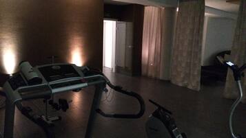 Une pièce équipée d’un tapis de course et d’un vélo elliptique, une porte donnant sur une autre pièce et un rideau.