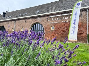 A brick building with a sign for 'de Brabantse restaurant - hotel' and a banner for 'Gastvrij Ambassadeur Land van de Peel.' - Herberg De Brabantse Kluis (Aarle-Rixtel)