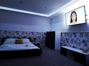 A bedroom with a bed, a TV mounted on the wall, a dresser, and a bench. - Hotel Tara (Kielce)