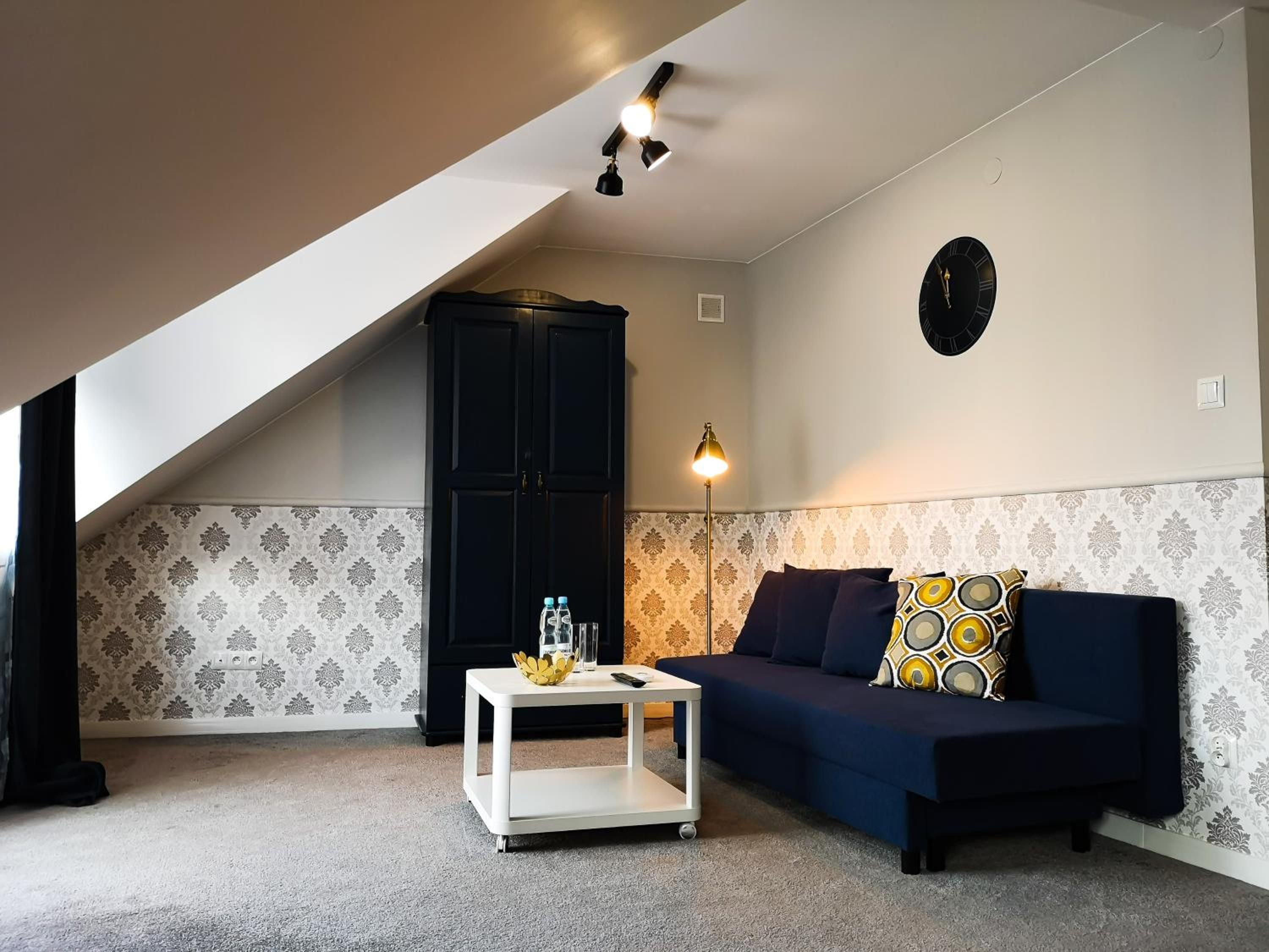 A room with a dark blue sofa, a white coffee table, a black cabinet, and patterned wallpaper.