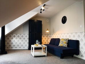 A room with a dark blue sofa, a white coffee table, a black cabinet, and patterned wallpaper.