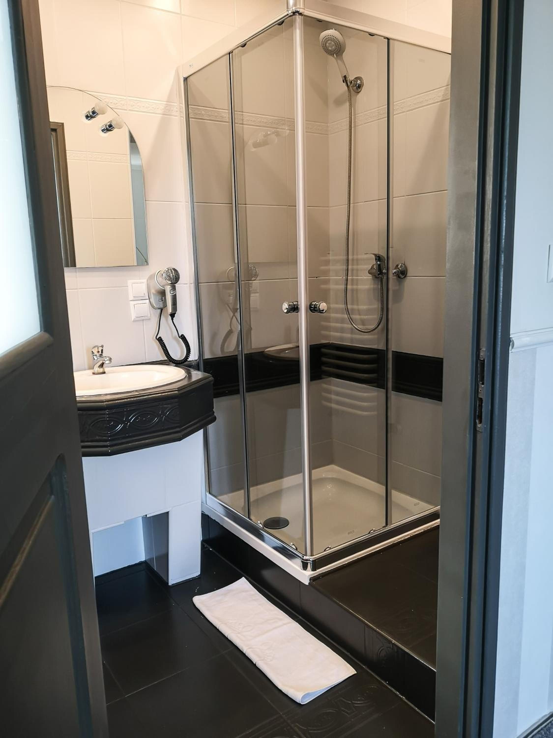 A modern bathroom with a glass-enclosed shower, a sink with a hairdryer, and a mirror.