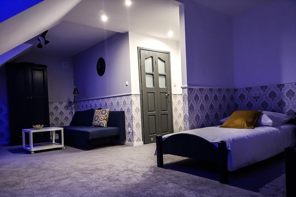A bedroom with a bed, a sofa, a small table, and a door.