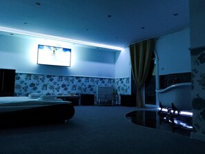 A hotel room with a bed, a flat-screen TV mounted on the wall, a mirror, and a window with curtains.