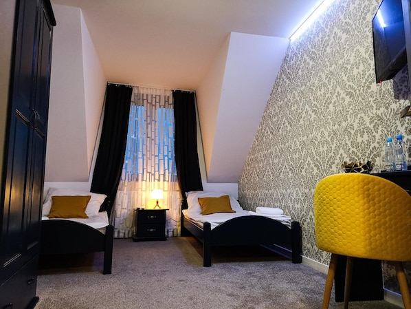 A bedroom with two beds, a nightstand, a lamp, a chair, and a TV.