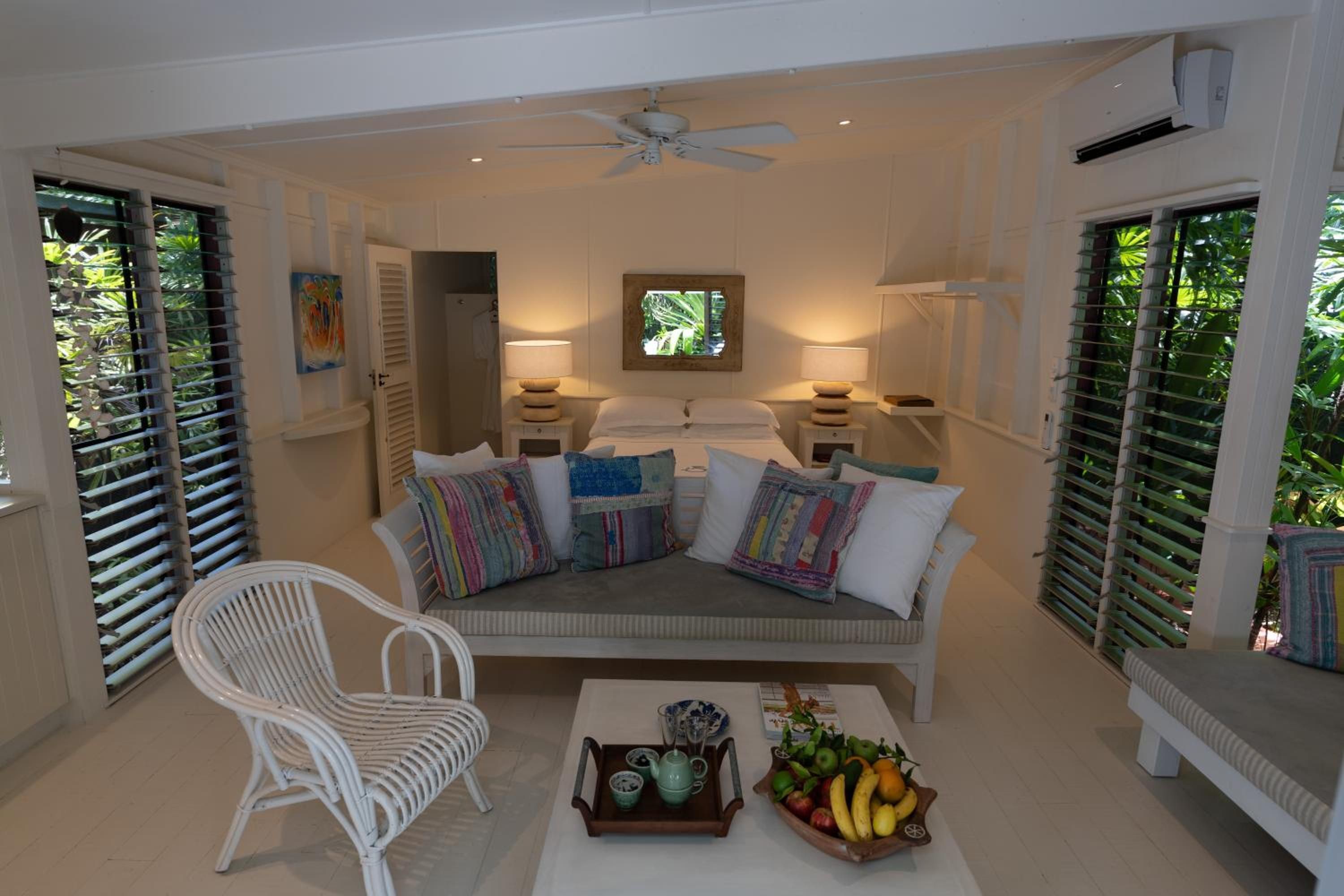 A room with a sofa, a chair, a table with a fruit bowl, and a ceiling fan.