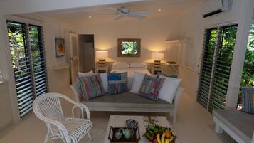 A room with a sofa, a chair, a table with a fruit bowl, and a ceiling fan.