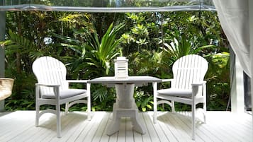 A white outdoor seating area with two chairs and a table, surrounded by lush greenery.