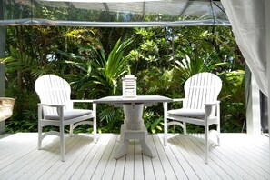 A white outdoor seating area with two chairs and a table, surrounded by lush greenery.