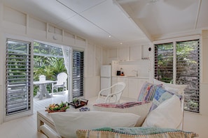 A room with a bed, a small table with a fruit bowl, a chair, and a kitchenette area.