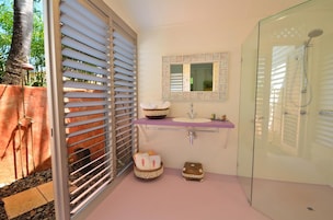 A bathroom with a glass shower enclosure, a sink with a mirror above it, and a window with blinds.