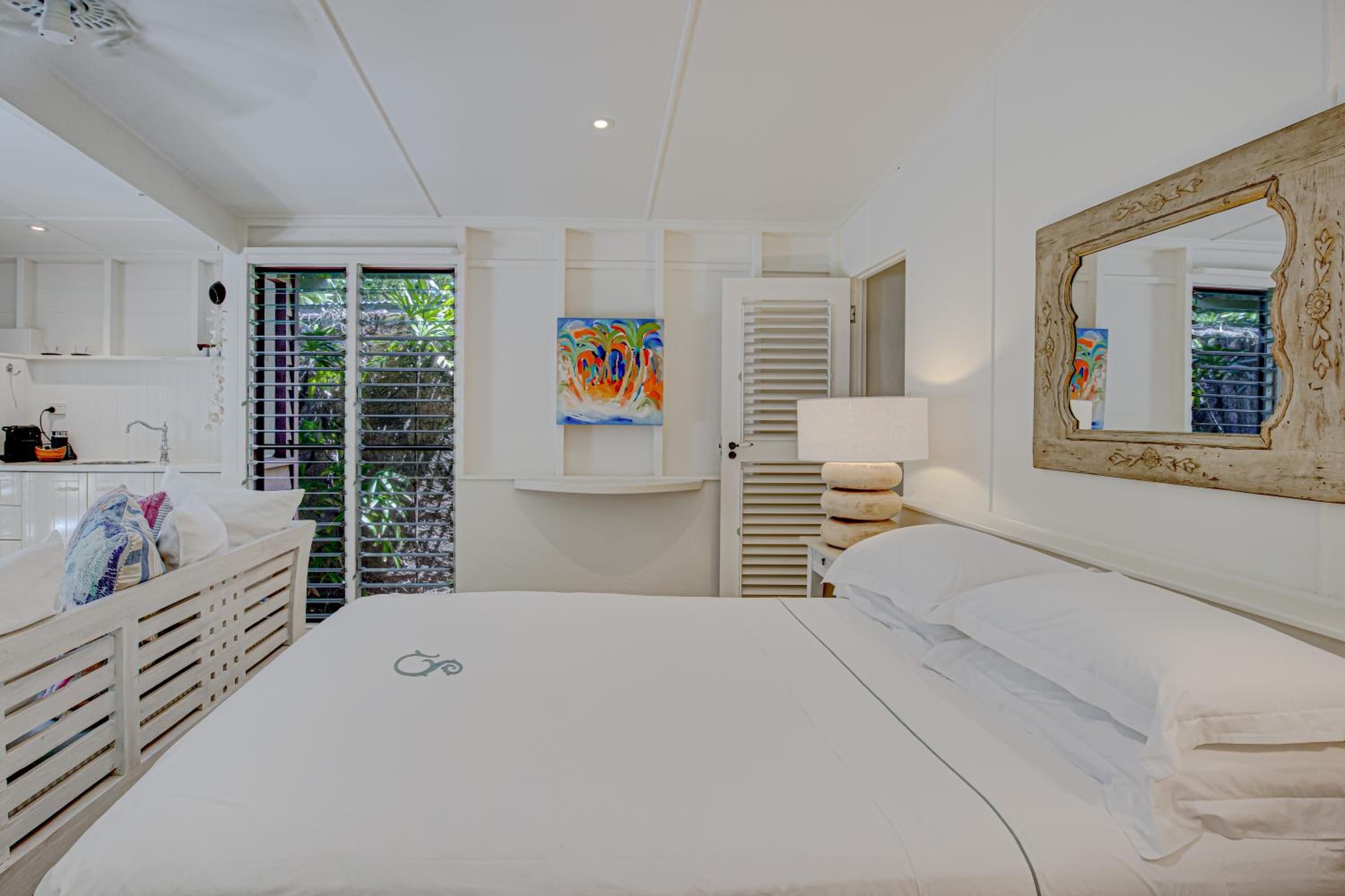A hotel room with a bed, a bathroom, a painting, and a view of greenery.