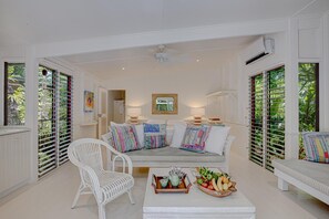 A room with a white sofa, a white chair, and a table with fruit and drinks.