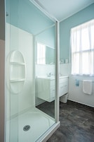 Un baño moderno con ducha envuelta en vidrio, un lavabo blanco y un espejo grande.
