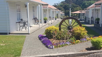 A row of white buildings with a covered patio area, a large wooden wheel, and a variety of flowers.