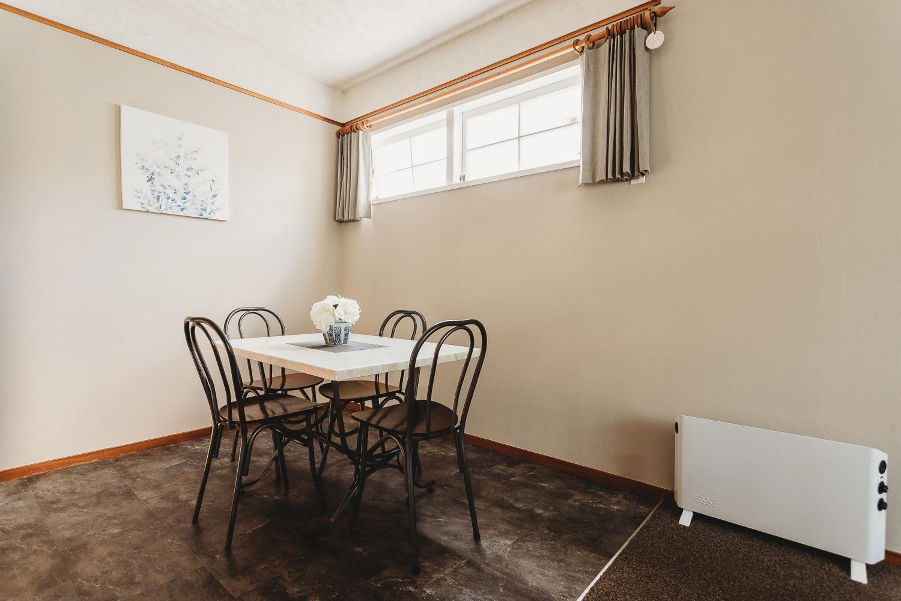 A dining area with a table and chairs, a radiator, and a window with curtains.