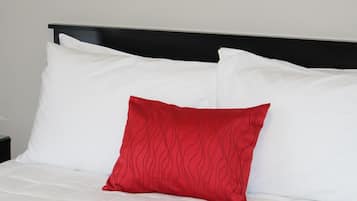 A bed with white bedding and a single red pillow.
