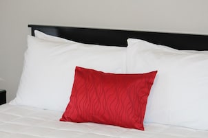 A bed with white bedding and a single red pillow.