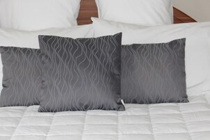 Una cama con ropa blanca y tres almohadas grises de diseño ondulado.