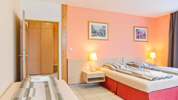 A hotel room with a bed, a bedside table, a nightstand, a wardrobe, and two framed pictures on the wall.