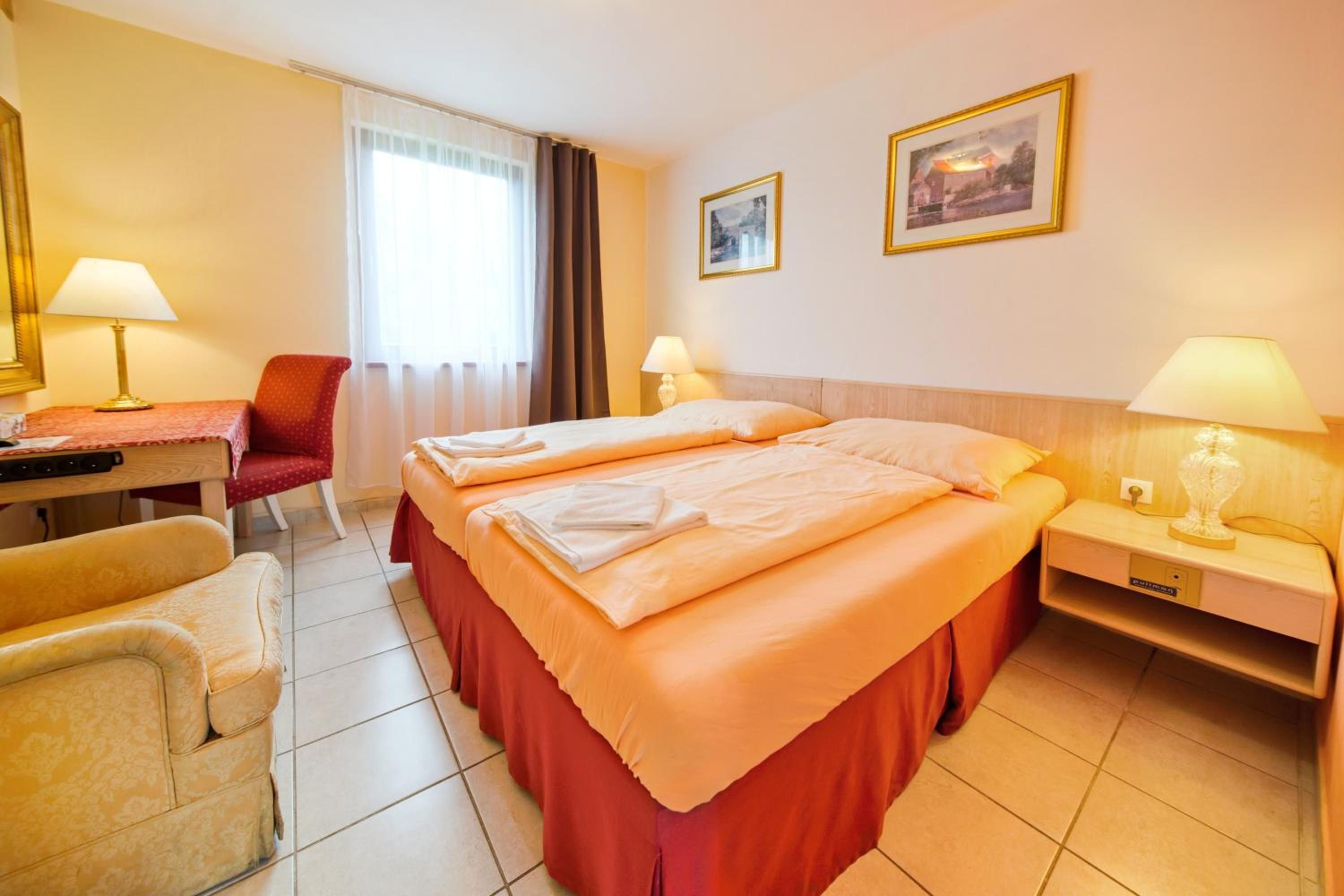 A hotel room with two beds, a desk, a chair, and two bedside tables with lamps.