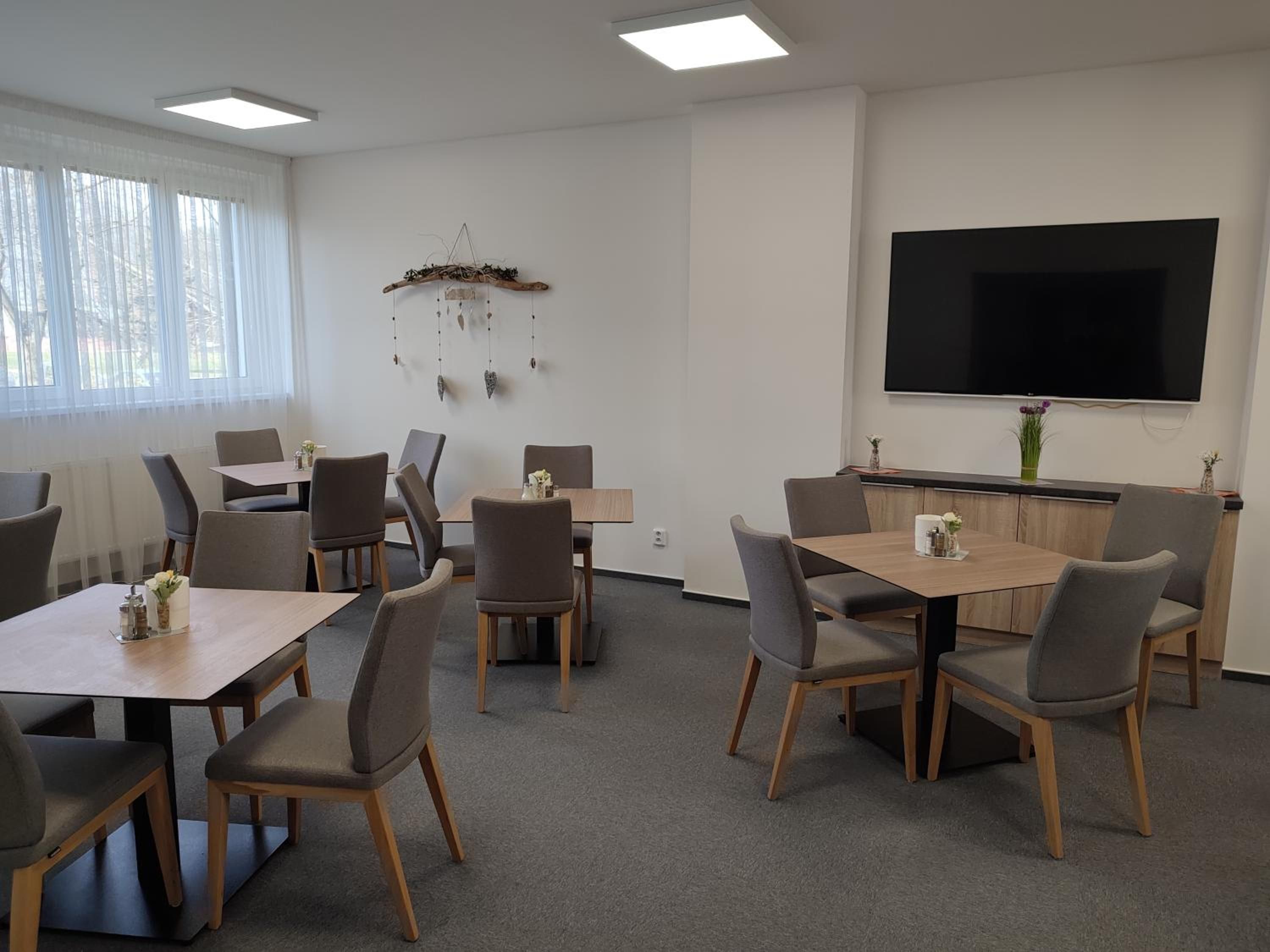 Un salón de conferencias con una pantalla plana grande, varias mesas y sillas, y un adorno decorativo en la pared.