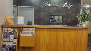 A reception desk with a sign reading 'Rosebank Lodge' and a display of local newspapers.