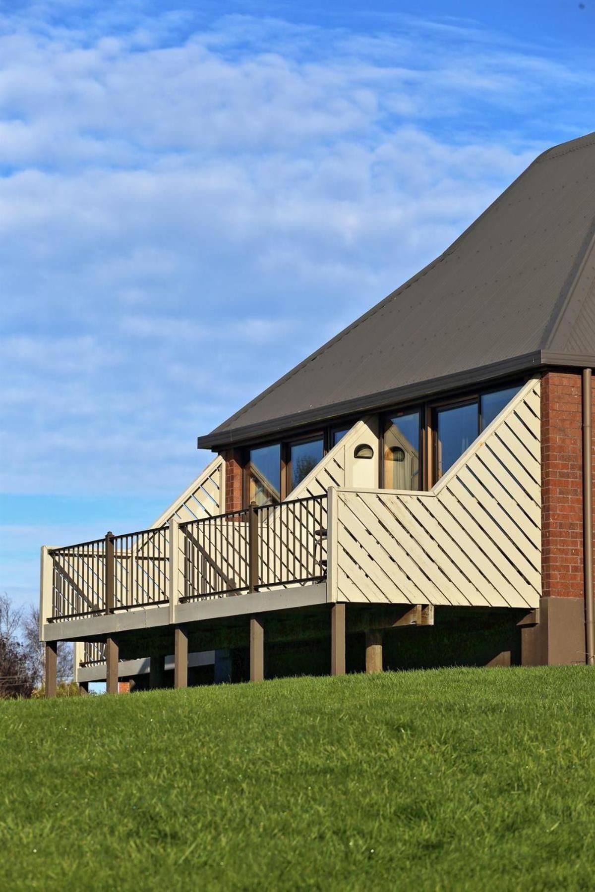 A modern building with a flat roof, a balcony with a metal railing, and a brick wall.