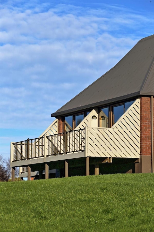 A modern building with a flat roof, a balcony with a metal railing, and a brick wall.