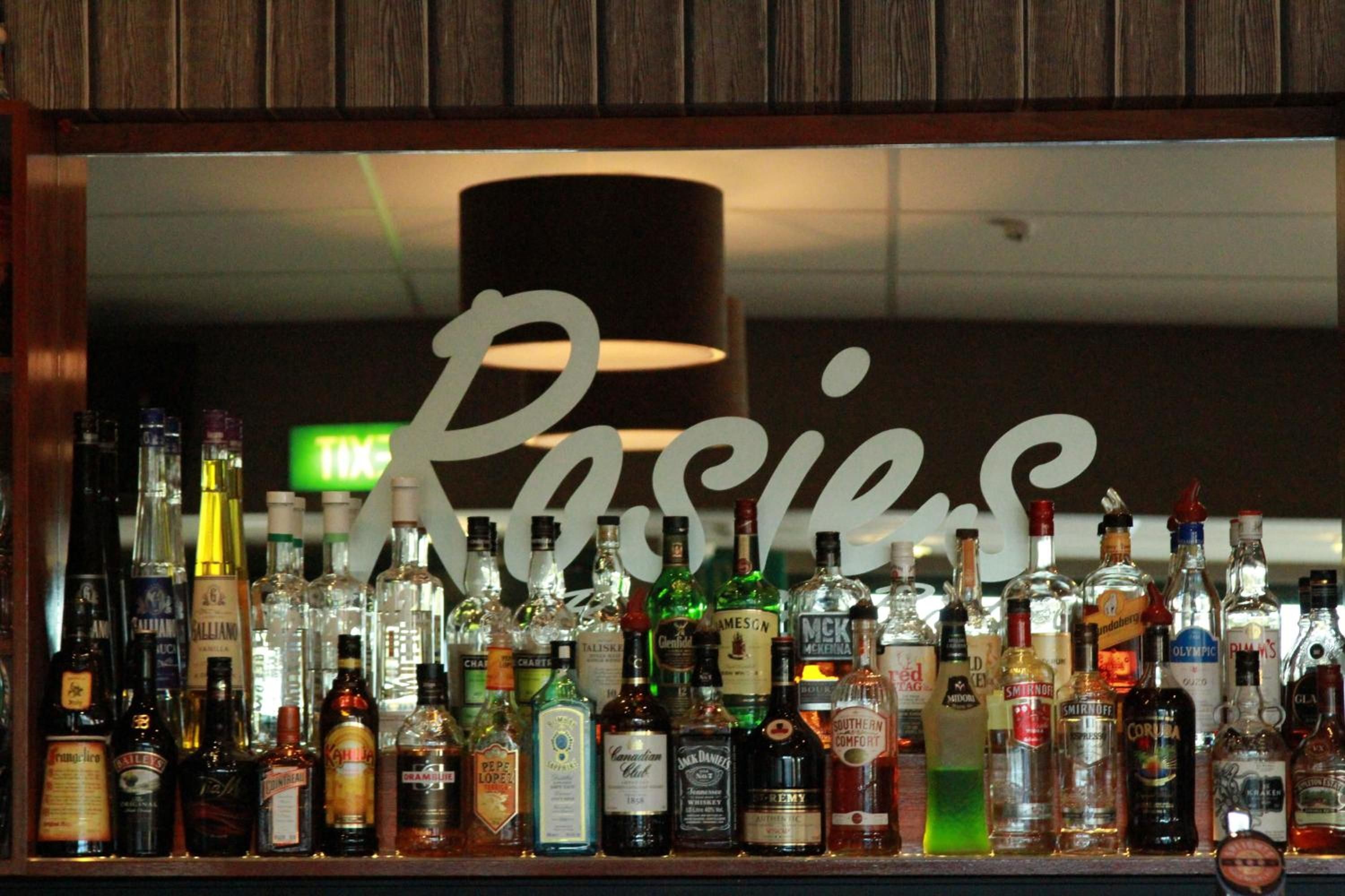 A bar with a variety of liquor bottles and a large sign with the word 'Rosies' in the background.