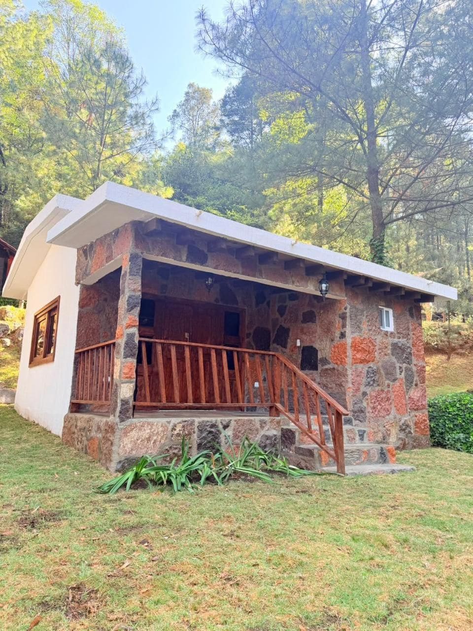 Edificio de piedra con porche y baranda de madera, rodeado de árboles.