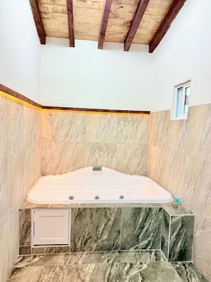 A bathroom with a marble floor, a bathtub, and a small window.