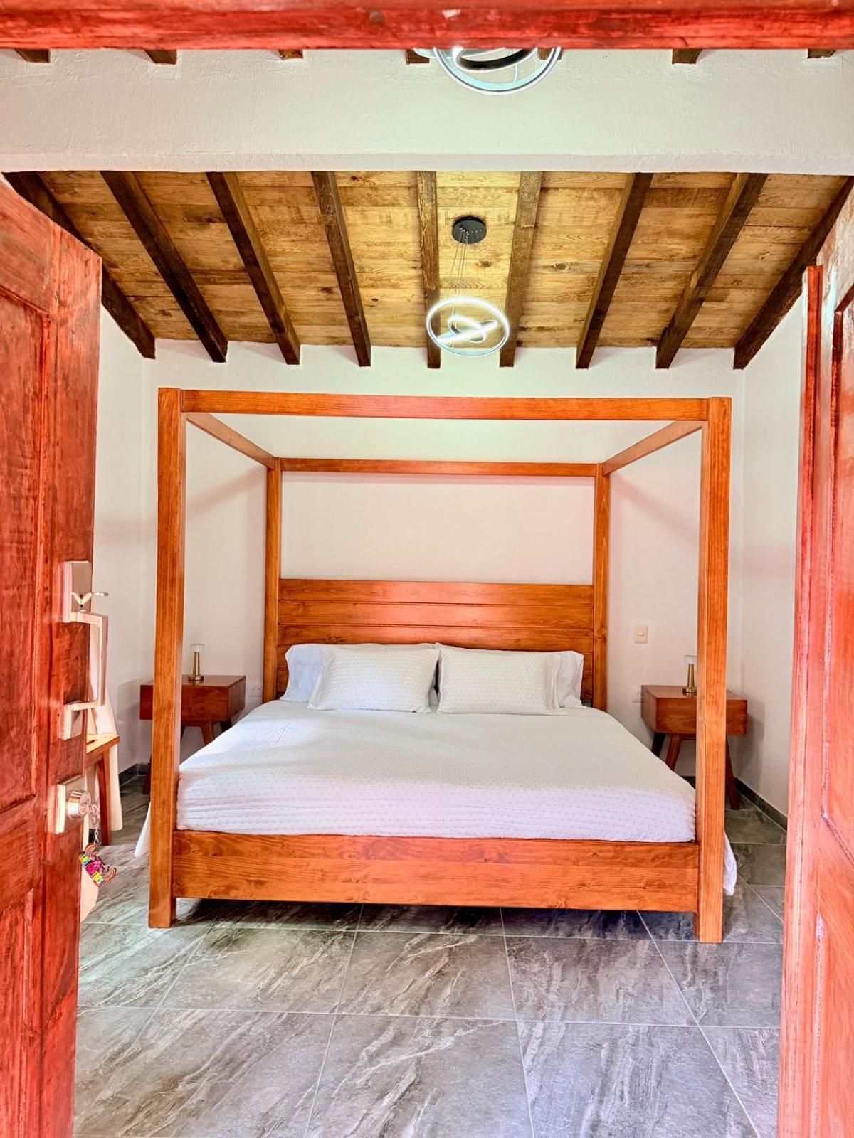 Una cama con dosel de madera con un colchón blanco, ubicada en una habitación con piso de piedra y techo de madera.