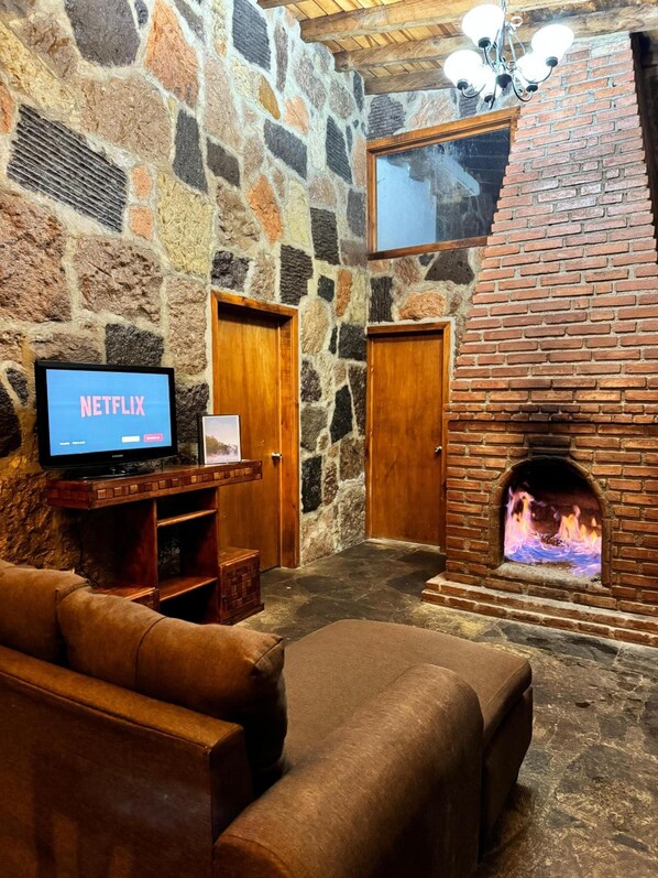 Una habitación de paredes de piedra con chimenea, televisor y sofá.