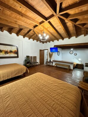 Una habitación con vigas de madera, un candelabro, un televisor y una chimenea.