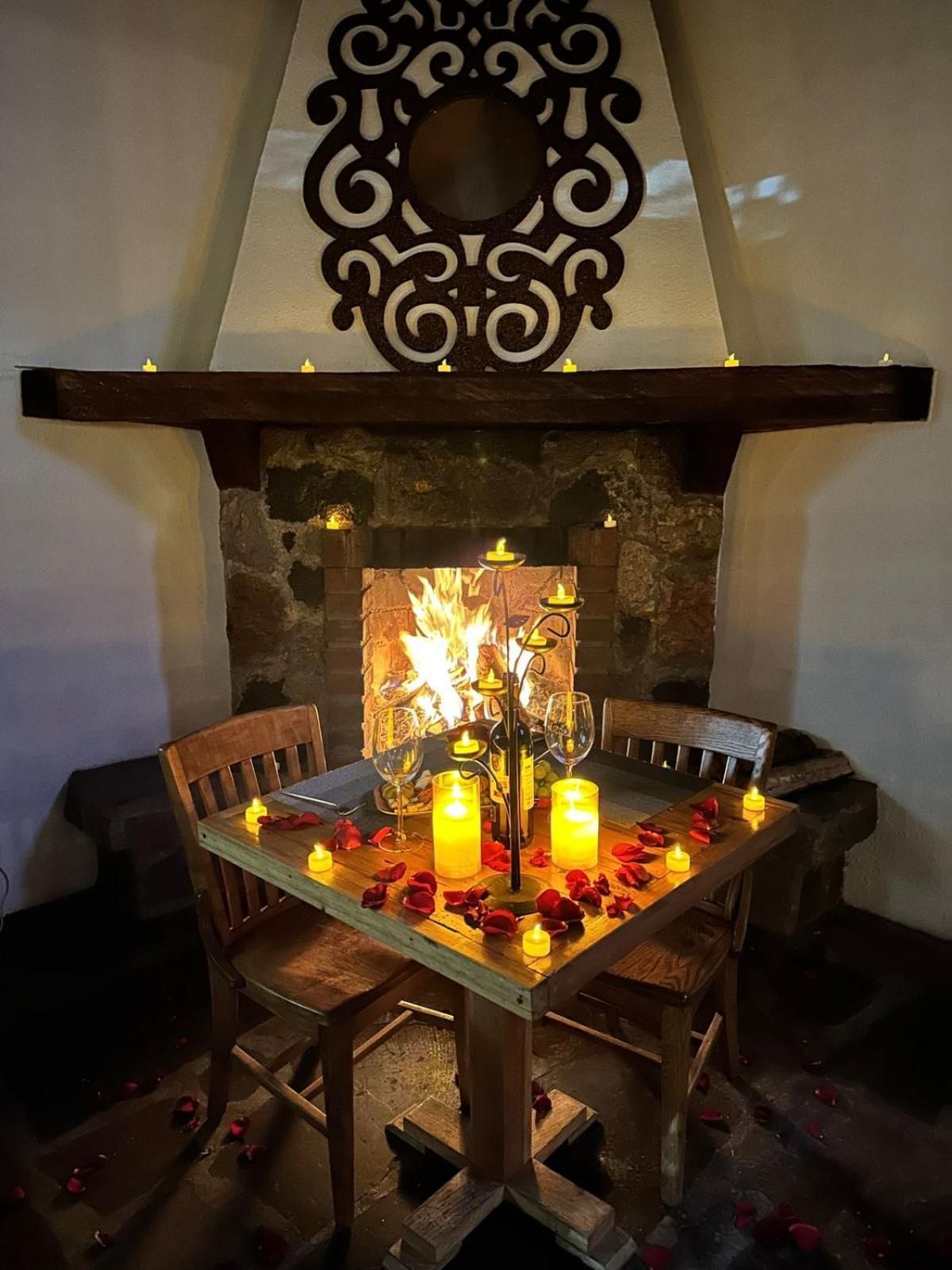 Una chimenea con repisa de piedra, una mesa con velas y sillas.