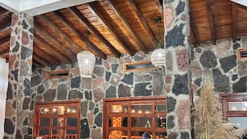 Un interior rústico con paredes de piedra, vigas de madera y una columna de piedra con un florero.