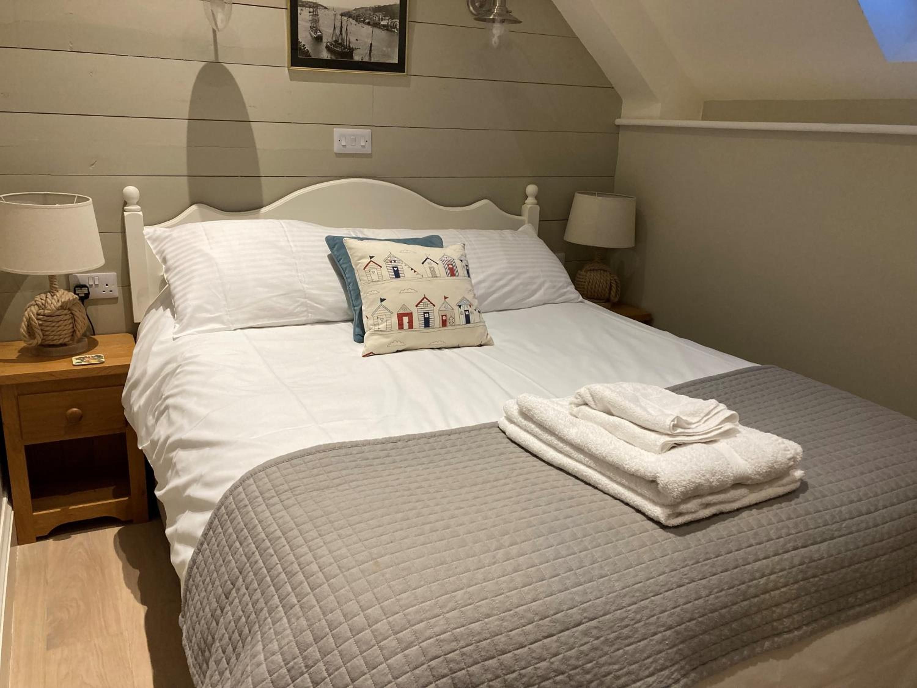 A neatly made bed with a quilted bedspread, a decorative pillow, and folded towels on a wooden nightstand.
