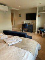 A hotel room with a bed, a desk, a chair, a television, and a wardrobe.
