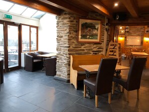 Interior de restaurante con paredes de piedra, mobiliario de madera y vistas amplias a través de grandes ventanales.