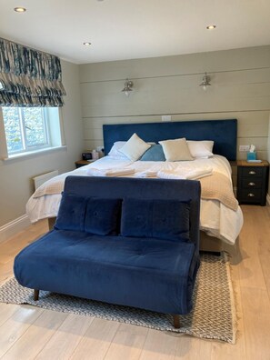 Un dormitorio con cama, mesitas de noche, una ventana y un banco tapizado en azul.