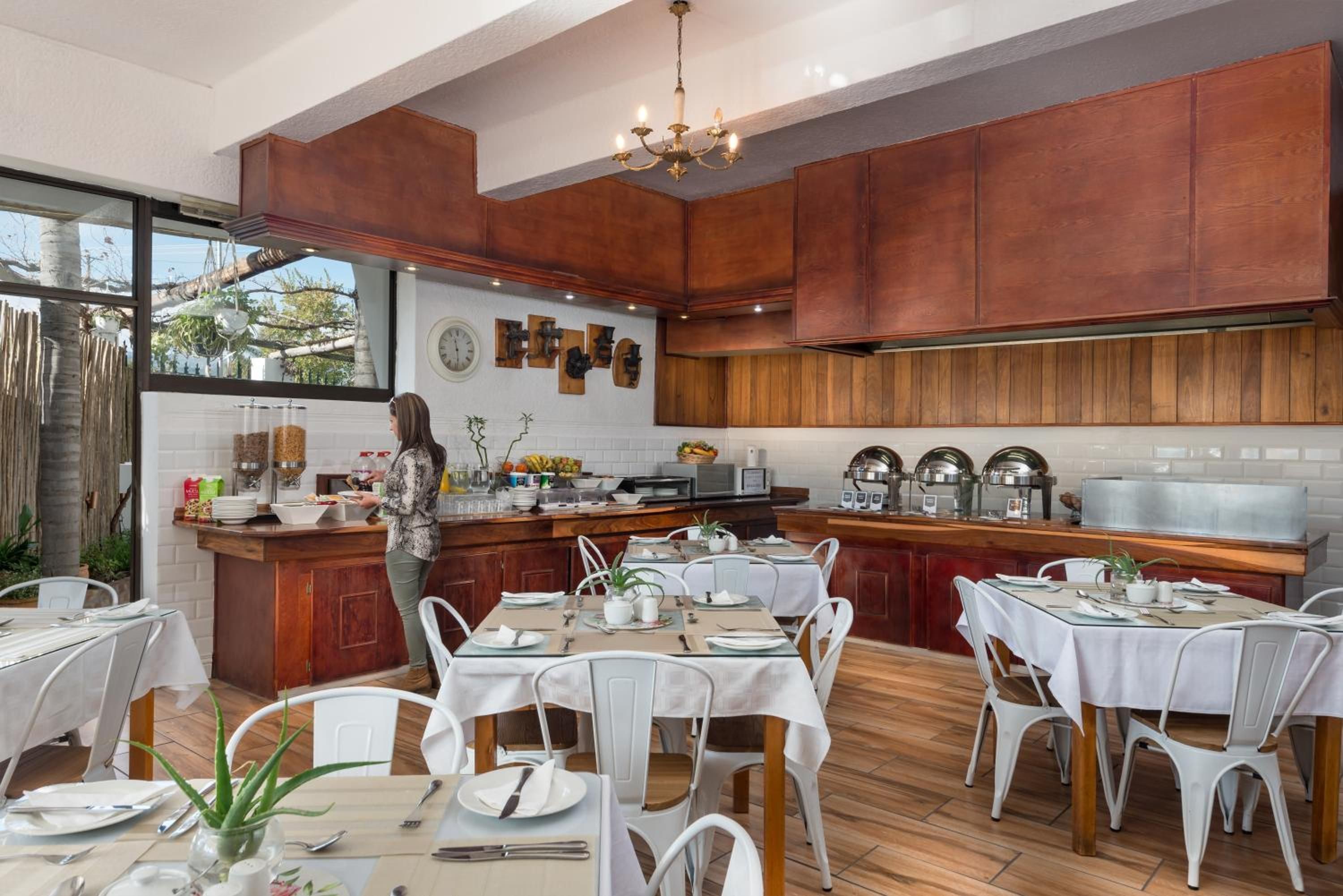 A modern kitchen with wooden cabinets, a central island, and a dining area with white chairs and tables.