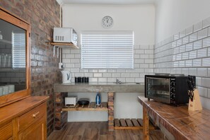 A compact kitchen with a brick wall, white tiled backsplash, a built-in microwave, a toaster oven, and a wooden countertop.