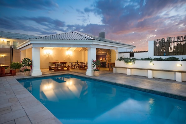 A modern outdoor pool area with a covered seating area and a fire feature. - Citrusdal Country Lodge (Cederberg)