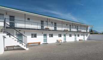 Un edificio de dos pisos con un espacio exterior cubierto, una escalera y varias ventanas.