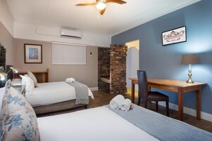 Habitación de hotel con dos camas, un escritorio, una silla, una lámpara, un ventilador de techo y una pared de ladrillo.