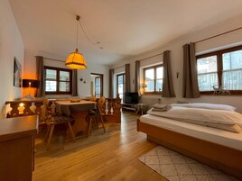 Habitación de hotel con cama, escritorio, silla, televisor y ventanas amplias.