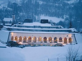 Edificio cubierto de nieve, con una piscina en primer plano y una iglesia al fondo.