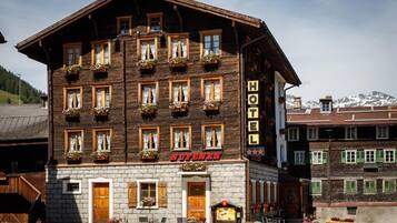 A hotel with a traditional wooden facade, multiple windows with flower boxes, and a sign indicating it is a hotel.